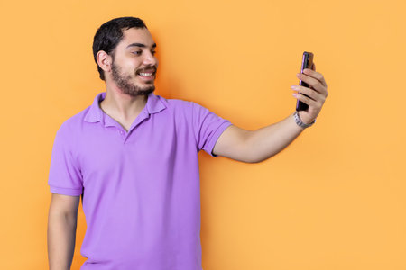 Bearded man, smiling, taking a picture with his smart phone, on orange background.の写真素材