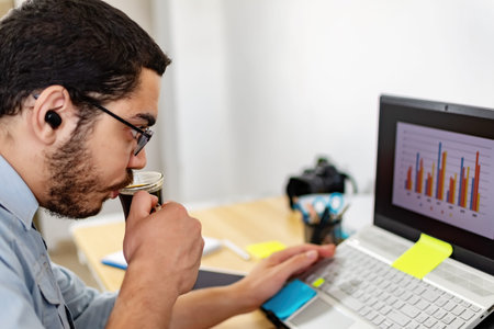 Businessman analyzing statistic on laptop while drinking coffee at office.