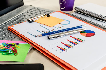 Office desk table with financial data, laptop, folder and cup of coffee.Top view. Supplies and...