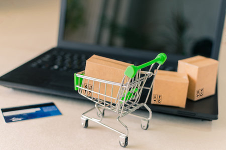 Close-up of a shopping cart with a box, next to a laptop and credit card, on the desk.の写真素材