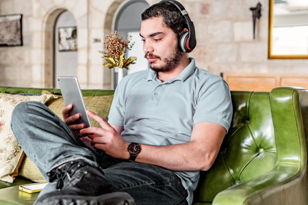 Happy man using a tablet to watch online content sitting on a couch at home.の写真素材