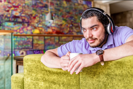 Man holding a coffee mug looking away, sitting on a couch in the living room at home.