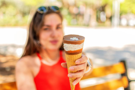 A woman's hand holds a chocolate waffle cone of ice cream on the background of a green nature park.
