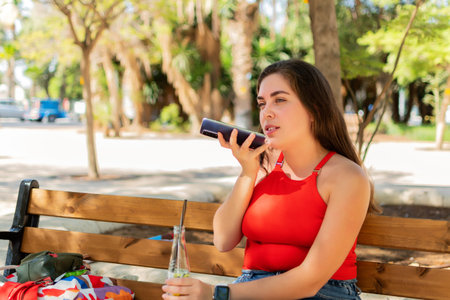 Woman recording audio message on phone in a park.