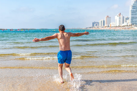 Young man running with arms open in clear blue sea.の写真素材