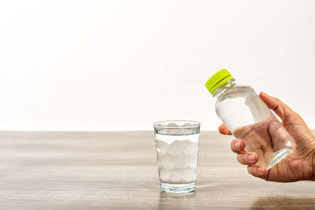 Female hand holding water bottle and glass on wooden table.の写真素材
