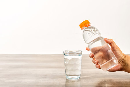Female hand holding water bottle and glass on wooden table.の写真素材