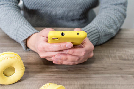 Female hand holding cell phone, wireless headphones on wooden table.の写真素材