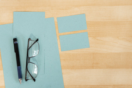Top view of office work space, wooden desk table with eyeglasses, blue textured paper and business...