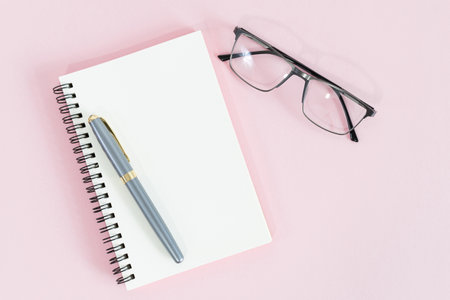 Blank notebook paper and pen on pink table background.の写真素材