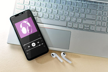 Smart phone with music app and laptop on desk, top view.
