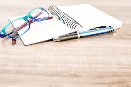 Notebook, pen and reading glasses on wooden table.の写真素材