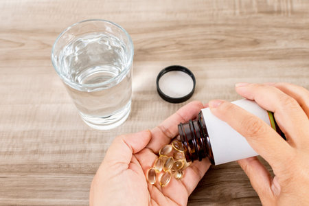 Female hand with pills and glass of water on wooden table.