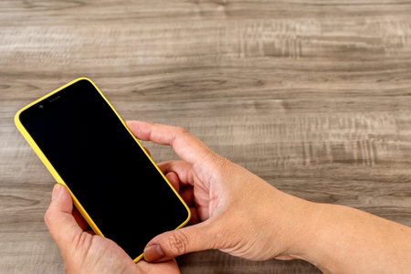 Female hand holding cell phone on wooden table.
