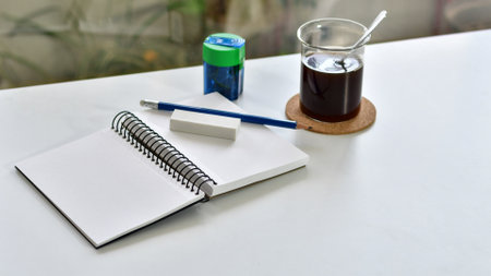 Desk with notebook, pencil, eraser and cup of coffee, next to a window.の写真素材
