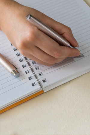 Close up of female hands writing in spiral notepad placed on white desktop, using an ink fountain pen.の写真素材