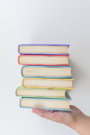 Female hand holding stacked books on white background. Study. Textbooks.の写真素材