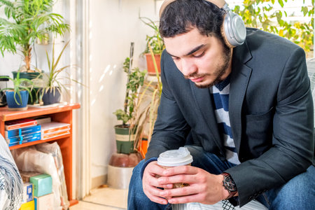 Young bearded man listening to music with wireless headphones, holding a coffee to go in paper cup.