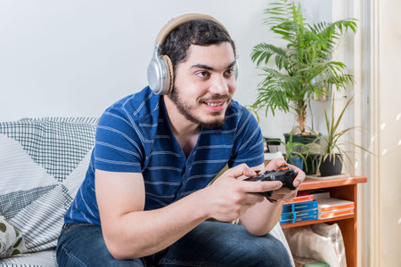 View of a happy young man playing the game, sitting on the sofa at home.