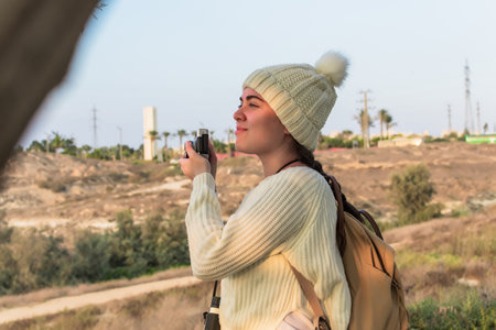 Woman outdoors using camera, taking photo in autumn, while sitting outside wearing warm down jacket. Pretty young Caucasian woman in active lifestyle.の写真素材