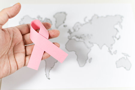 World Cancer Day, hand with pink ribbon symbol on blur gray world map background. Select focus. Soft ficus. top view. Medicine concept.の写真素材