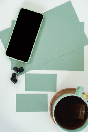 Cropped shot of male style, smart phone on green modern office desk with business card, tea cup, watch.の写真素材
