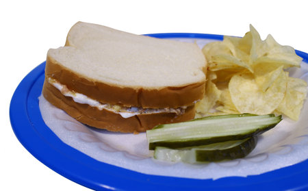 A deviled ham sandwich with pickles and potato chips on a paper plate with a holder isolated on white の写真素材