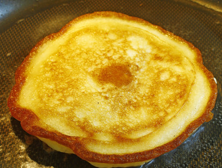 A fresh golden brown cooking breakfast pancake being cooked in grease creating a crispy edge in a...