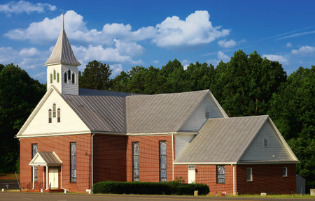 An old red brick church alongside the road near the edge of the woodsの写真素材