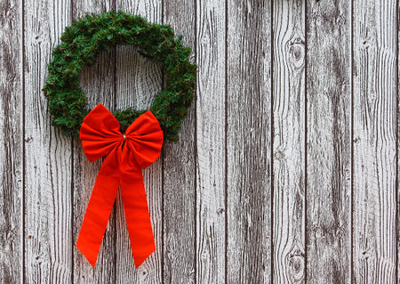 A large green Christmas Wreath with a large red Bow on it against a wooden styled background with room for your textの写真素材
