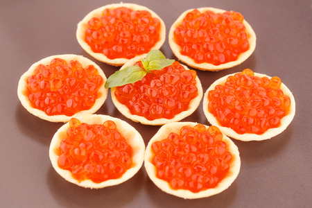Red caviar in round pastries on brown plate.の写真素材