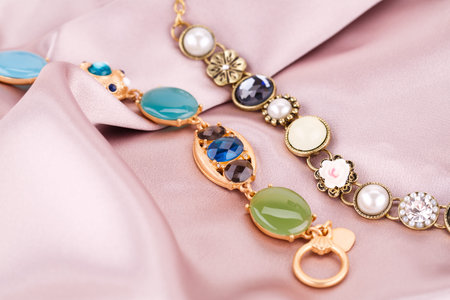 Stylish bracelets with pearls and stones on fabric background.