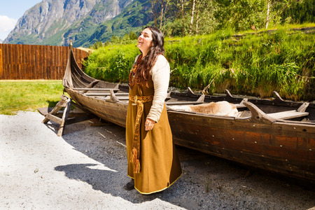Gudvangen, Norway - June 13 - The young woman in national clothes and longboat drakkar in the viking village museum.のeditorial素材