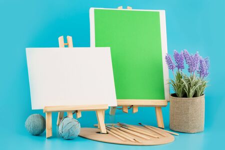 Two wooden blank easels with brushes and plant on blue background.の写真素材