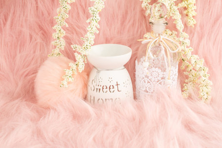 Home decorative with aroma lamp, decorative bottle and  white flowers on pink fur background.