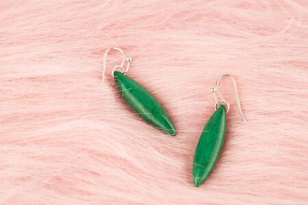 Stylish earrings with green stone on pink fur background.の写真素材