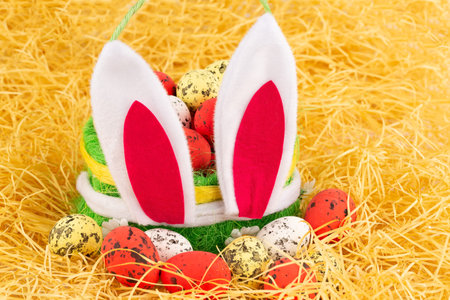 Easter colorful eggs in basket and bunny ears on yellow straw background.