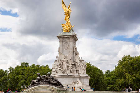 London, UK - August 8, 2019 -  Tourists sitting around Victoria Memorial with marble and bronze statues, iconic monument surrounded by gardens., in front of Buckingham Palace.のeditorial素材