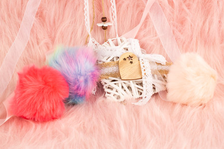 White wooden heart with ribbon and fluffy balls on pink fur background.の写真素材