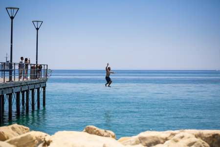 Limassol, Cyprus - July 9, 2021 - Unidentified young man walking on the rope above the sea, other people take photos by smartphone.のeditorial素材