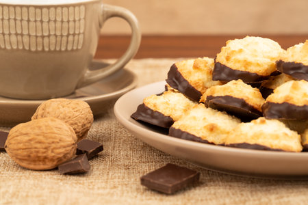 Coconut cookies on beige plate, cup of coffee, walnuts and chocolate on burlap  background.の写真素材