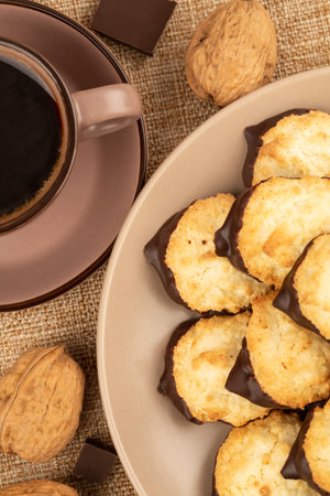 Coconut cookies on beige plate, cup of coffee, walnuts and chocolate on burlap  background.の写真素材