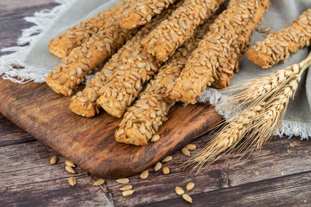 Bread sicks with sunflower seeds on wooden tray, wheat ears and grains.