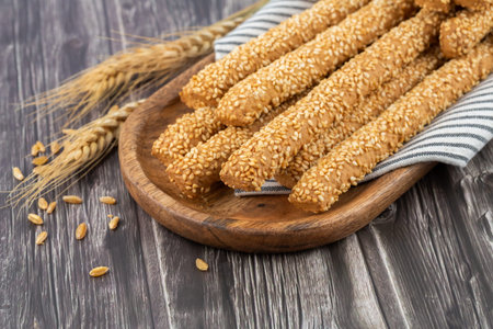 Bread sicks with sesame seeds on wooden tray. Wheat ears and grains.