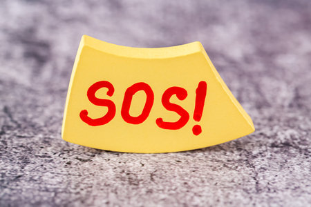 SOS word on the yellow wooden board on the gray background. SOS word with red letters. Close up image.の写真素材