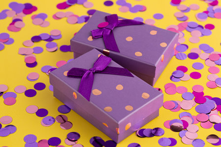 Two purple gift boxes with golden dots and purple ribbons on the yellow background. Round confetti on the yellow background.の写真素材