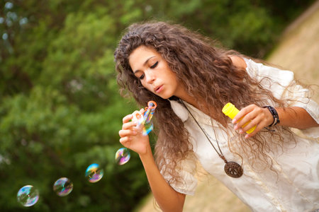Beautiful woman in the park playing in bubbles cup. Outdoor portrait.