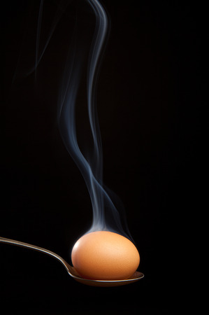Brown egg wrapped in smoke in silver spoon. Black background. Studio shotの写真素材