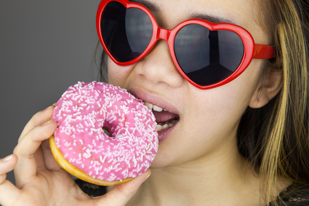 Sexy woman with red lolita glasses eating donut. Studio shotの写真素材