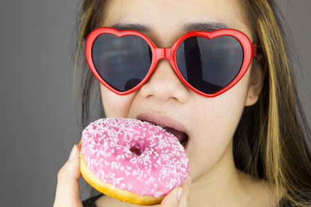 Sexy woman with red lolita glasses eating donut. Studio shotの写真素材